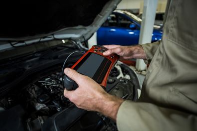 Technician standing in front of open car bonnet with diagnostic tool